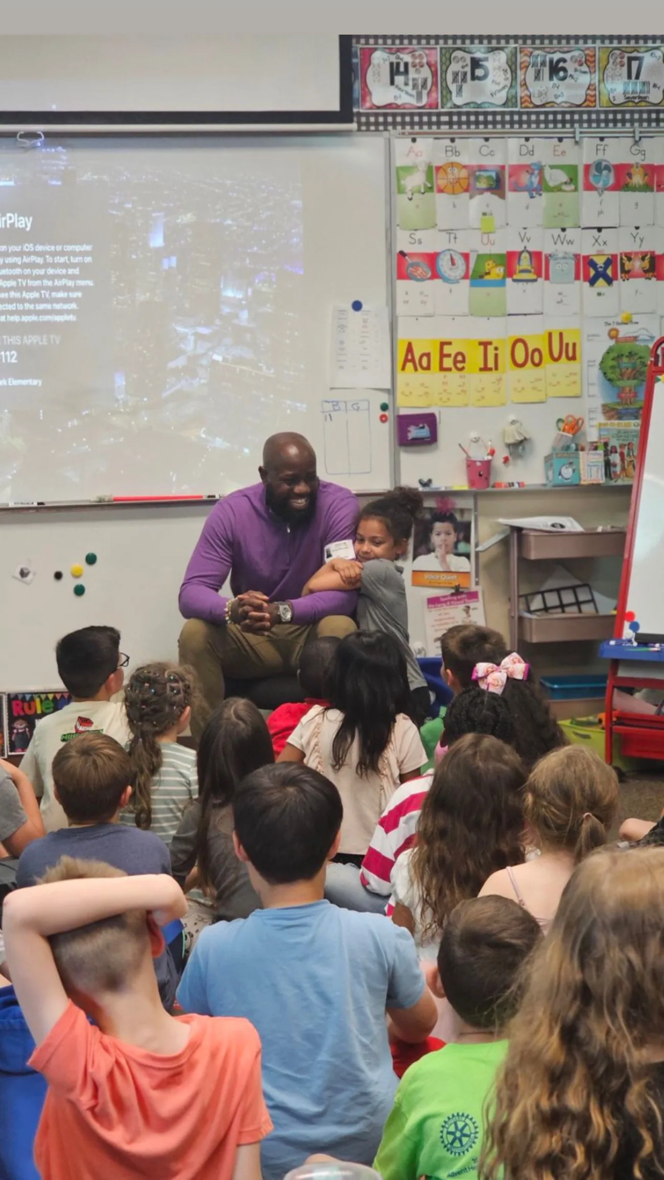 Hugo Maynard reading one of his books to a classroom of children seated on the floor