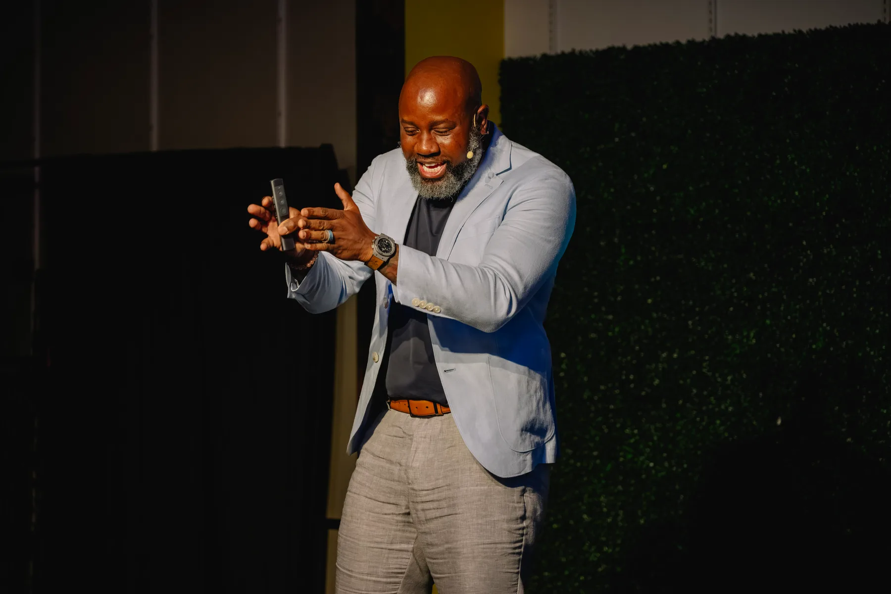 Hugo Maynard on stage mid-talk, presentation remote in hand, gesturing as he makes a point